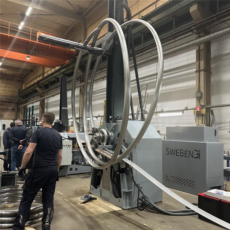 1 (1) Engineer inspecting a large-diameter bent tube on an industrial tube bending machine by SweBend, showcasing advanced tube bending technology in a manufacturing facility.