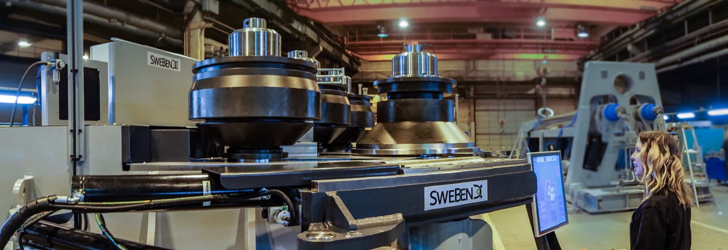 Operator at the SEVEN X touchscreen beside a SweBend section bender